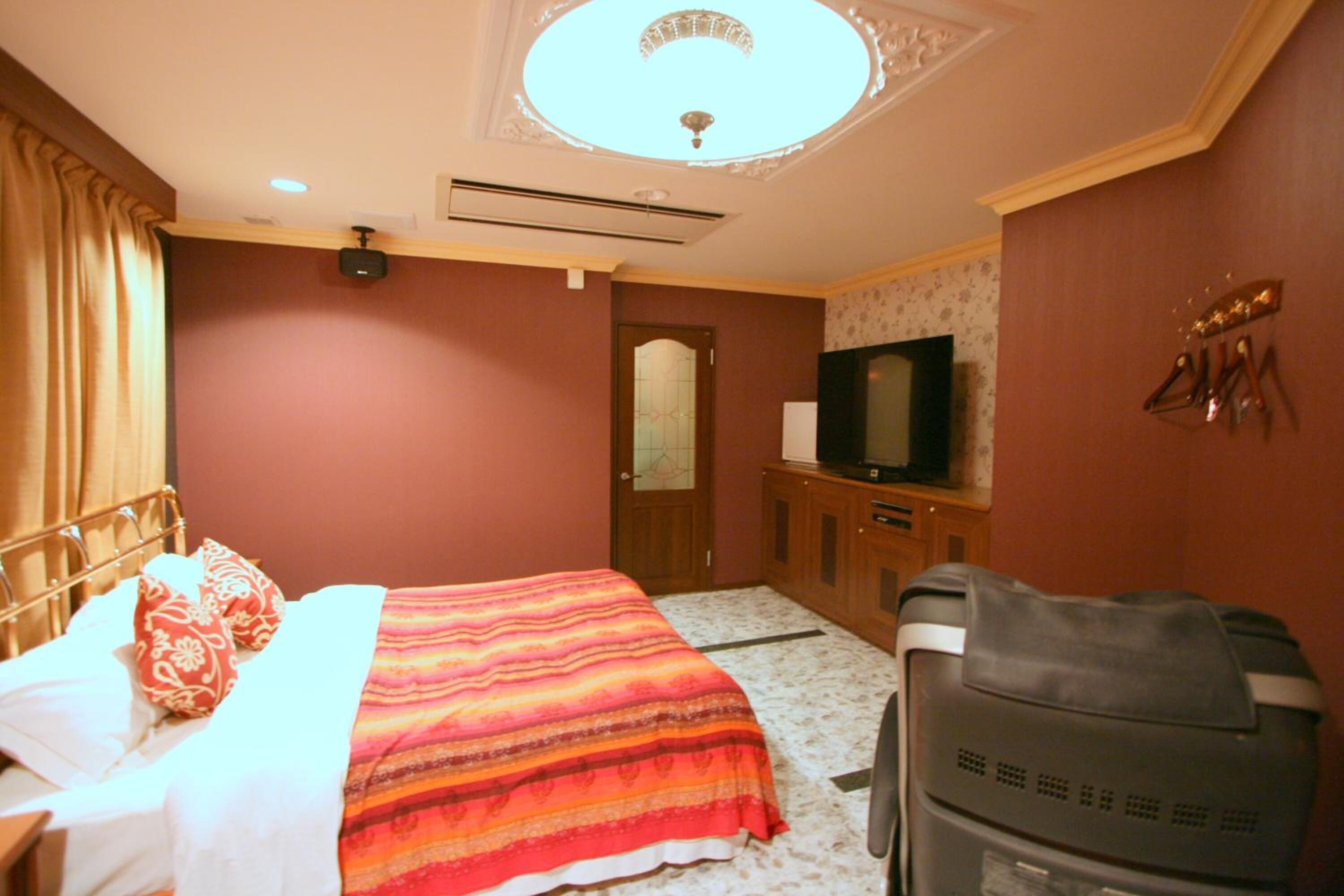 A hotel room with a bed, a television, a desk, and a suitcase.