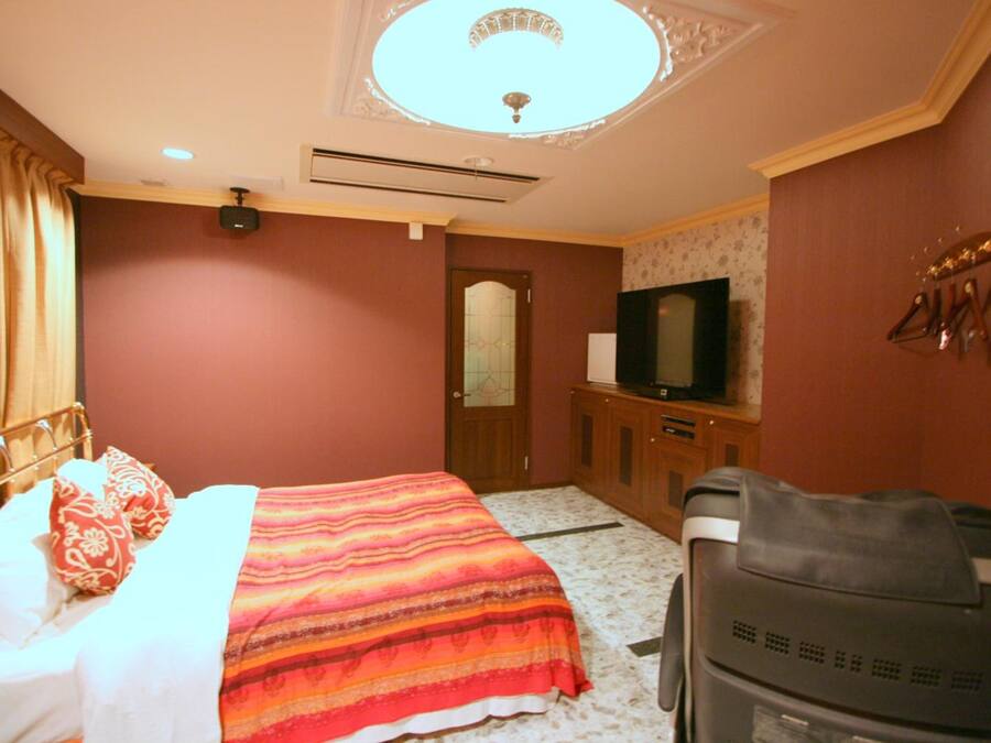 A hotel room with a bed, a television, a desk, and a suitcase.