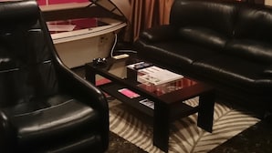 Ein Raum mit Massagegerät, zwei Ledersofas, einem kleinen Couchtisch und einem Deckenventilator.