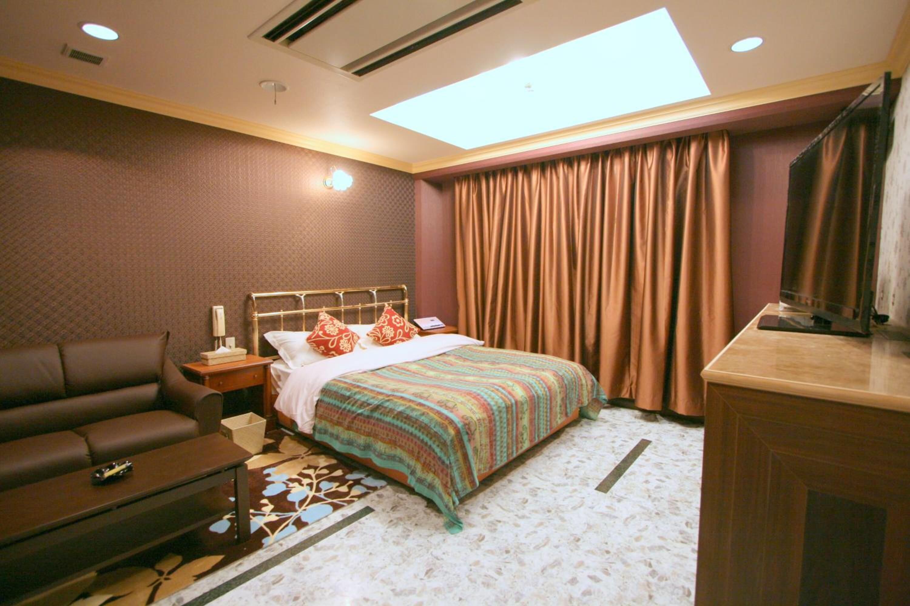 A hotel room with a bed, a sofa, a desk, and a large window with curtains.