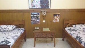 A room with two wooden beds, a small table with a telephone, and a wall adorned with framed pictures and a decorative item. - Handika Hotel Mataram (Mataram)