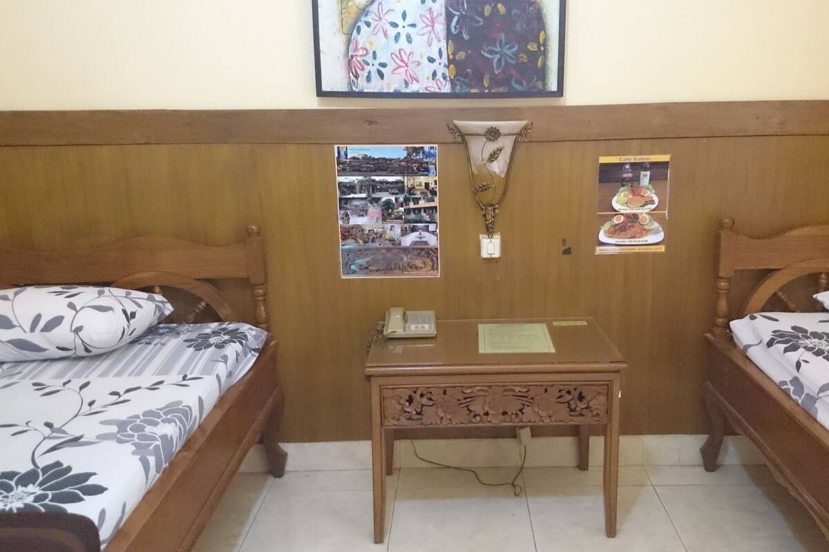 A room with two wooden beds, a small table with a telephone, and a wall adorned with framed pictures and a decorative item.