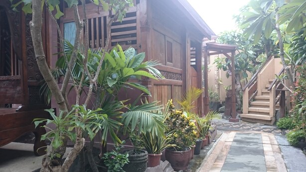 A wooden house with a porch, surrounded by potted plants and a staircase leading to a covered area. - Handika Hotel Mataram (Mataram)
