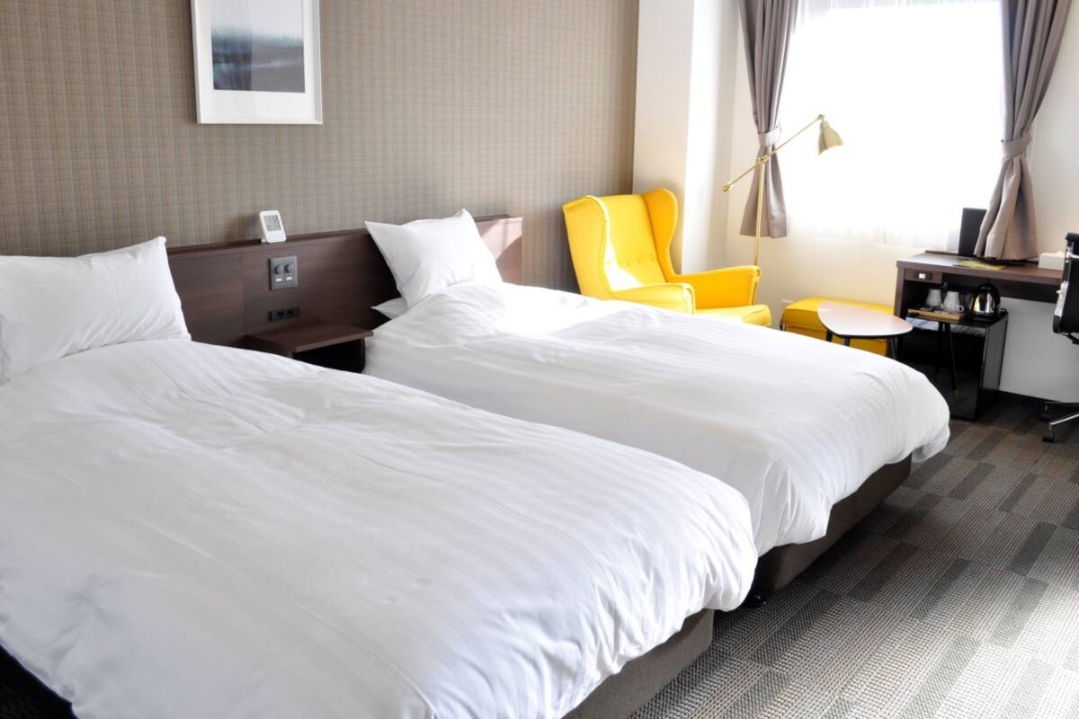 Une chambre d’hôtel avec deux lits, un bureau, une chaise et une lampe.