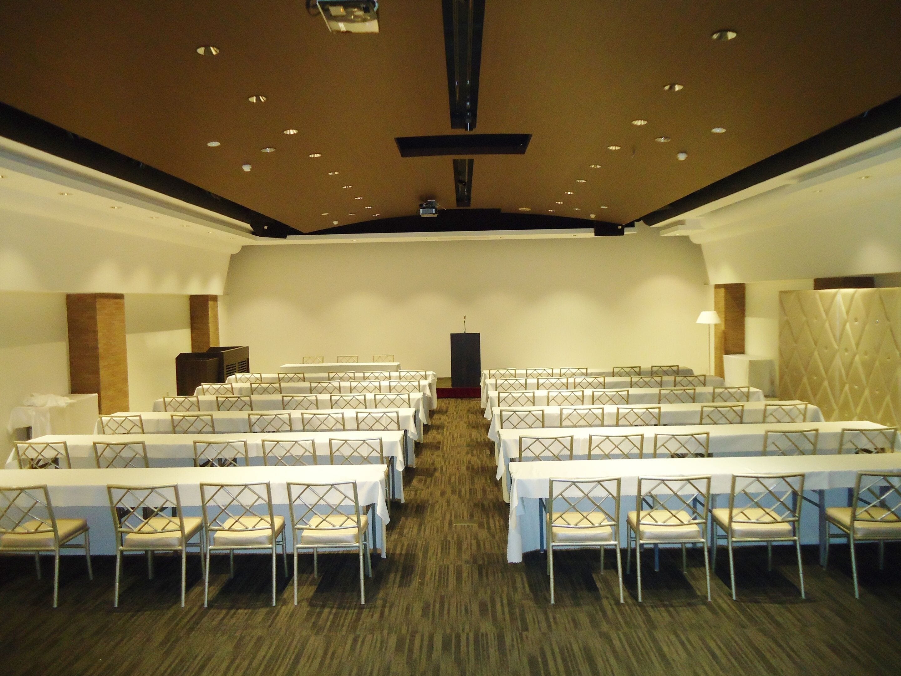 A conference room with rows of tables and chairs, a podium, and a carpeted floor.