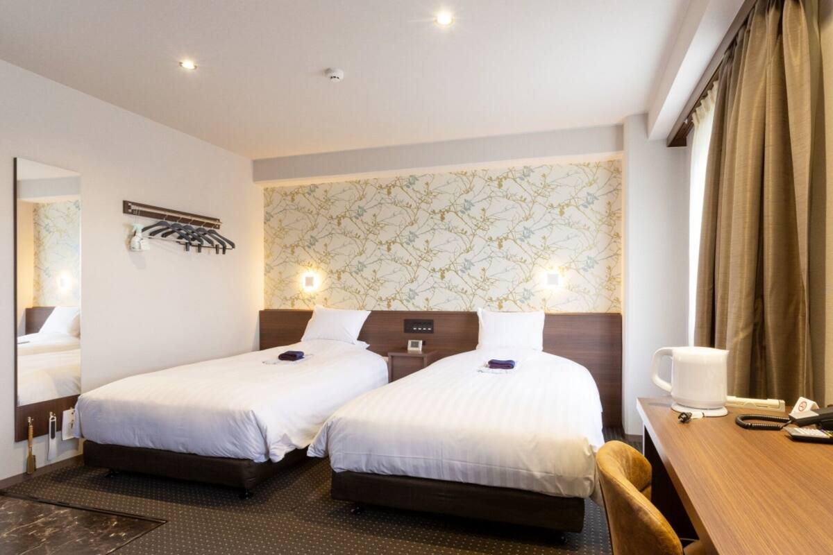 Une chambre d’hôtel avec deux lits simples, un bureau avec une chaise, une machine à café et un miroir.