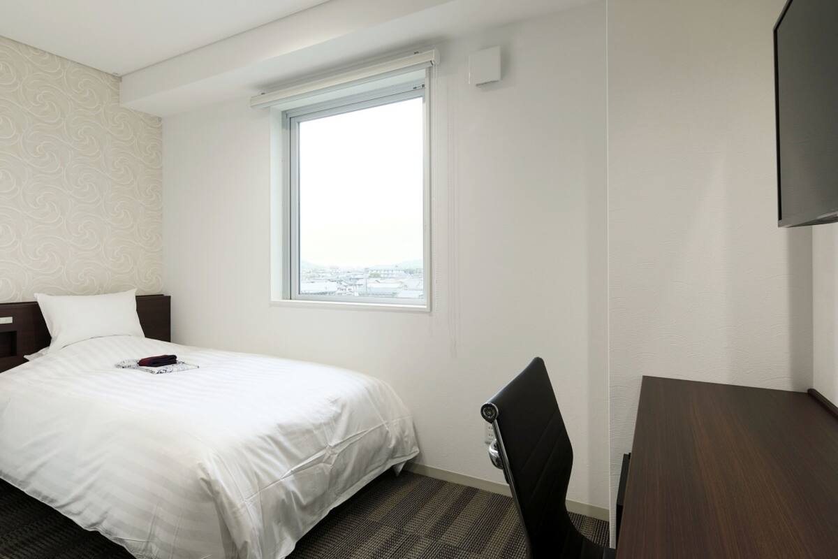 Une chambre d’hôtel équipée d’un lit, d’un bureau, d’une chaise, d’une fenêtre et d’un téléviseur à écran plat.