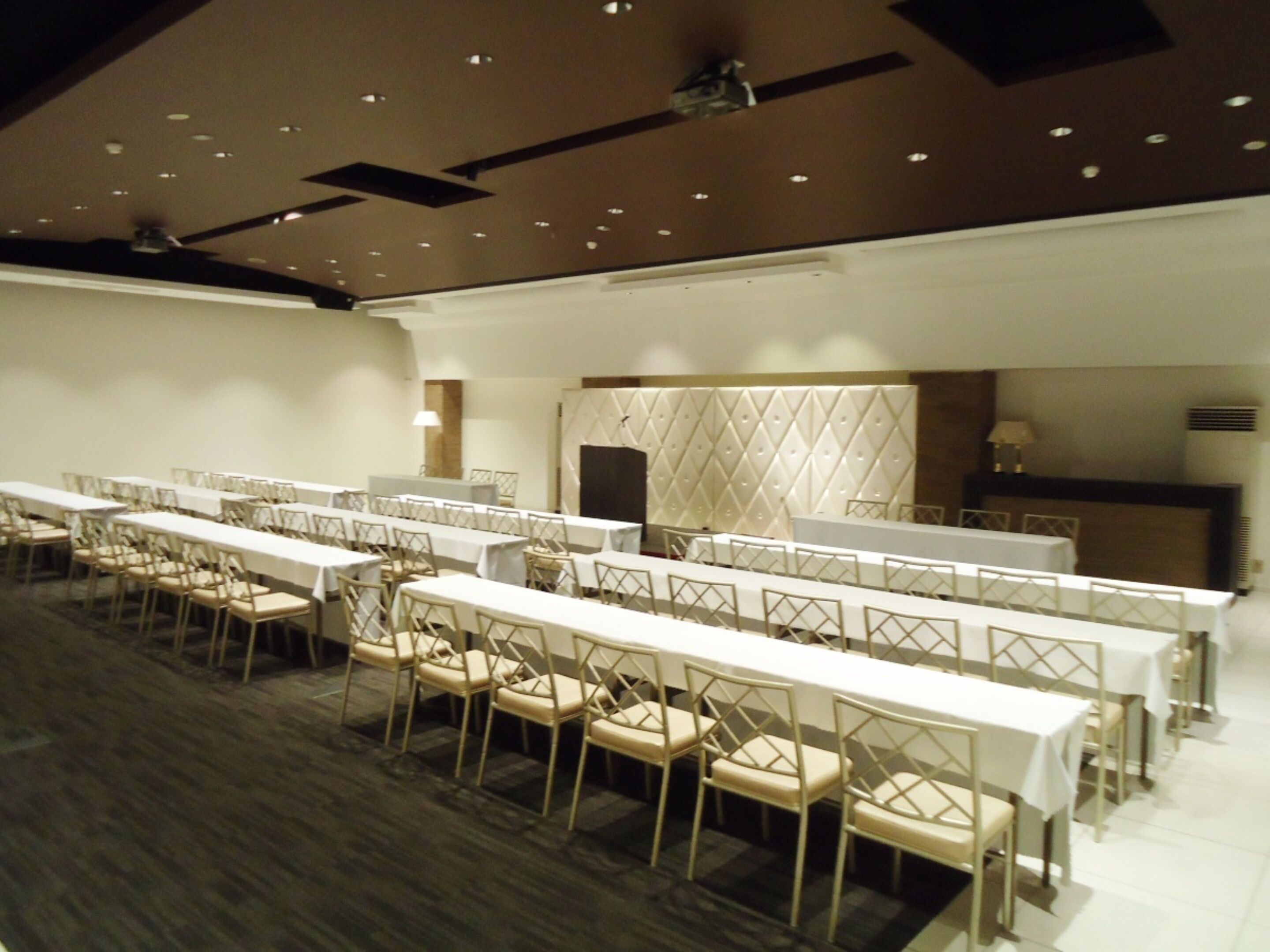 Een congreszaal met lange tafels en stoelen, een hoog plafond met inbouwverlichting en een decoratief paneel.