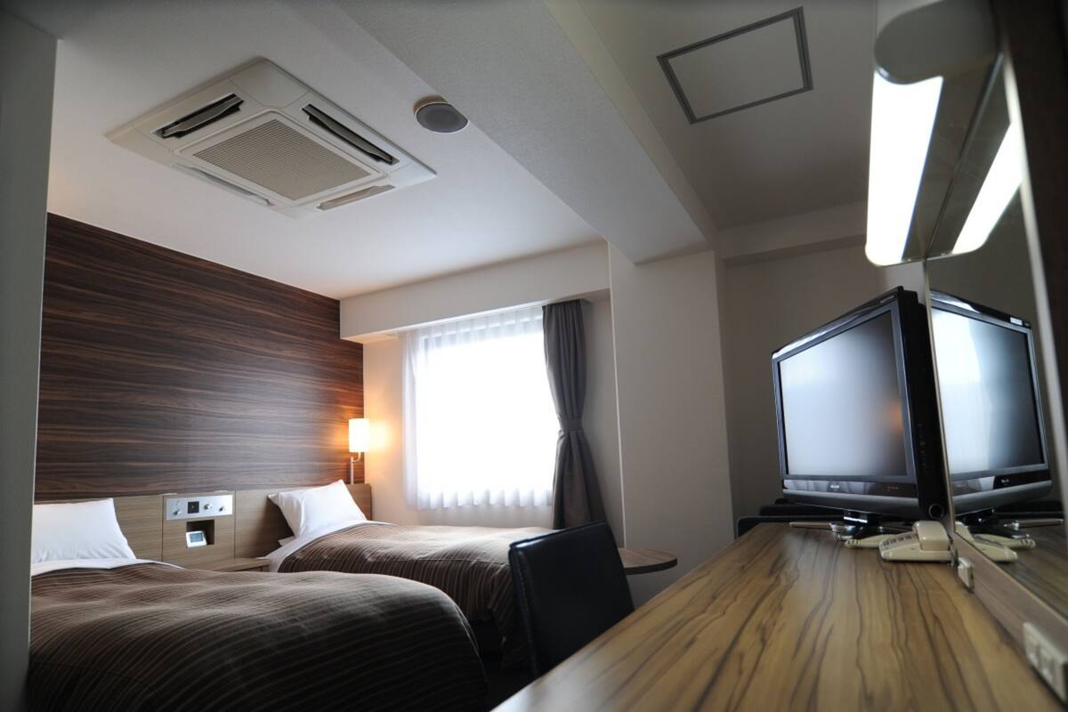 Une chambre d’hôtel avec deux lits, une tête de lit en bois, une télévision, un bureau et une lampe.