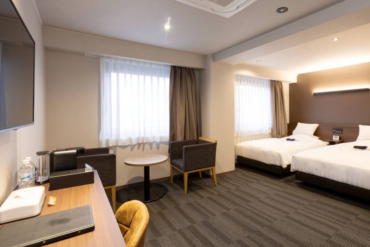 Une chambre d’hôtel avec deux lits, un bureau, une chaise, une petite table et un téléviseur.
