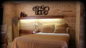 A room with a brick wall, a bed with a headboard, a nightstand with a lamp, and a decorative wall piece above the bed. - York Motel (York)