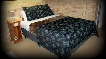 Een slaapkamer met een bakstenen muur, een houten nachtkastje met een lamp, een bed met een bloemenlaken en een hoofdbord.