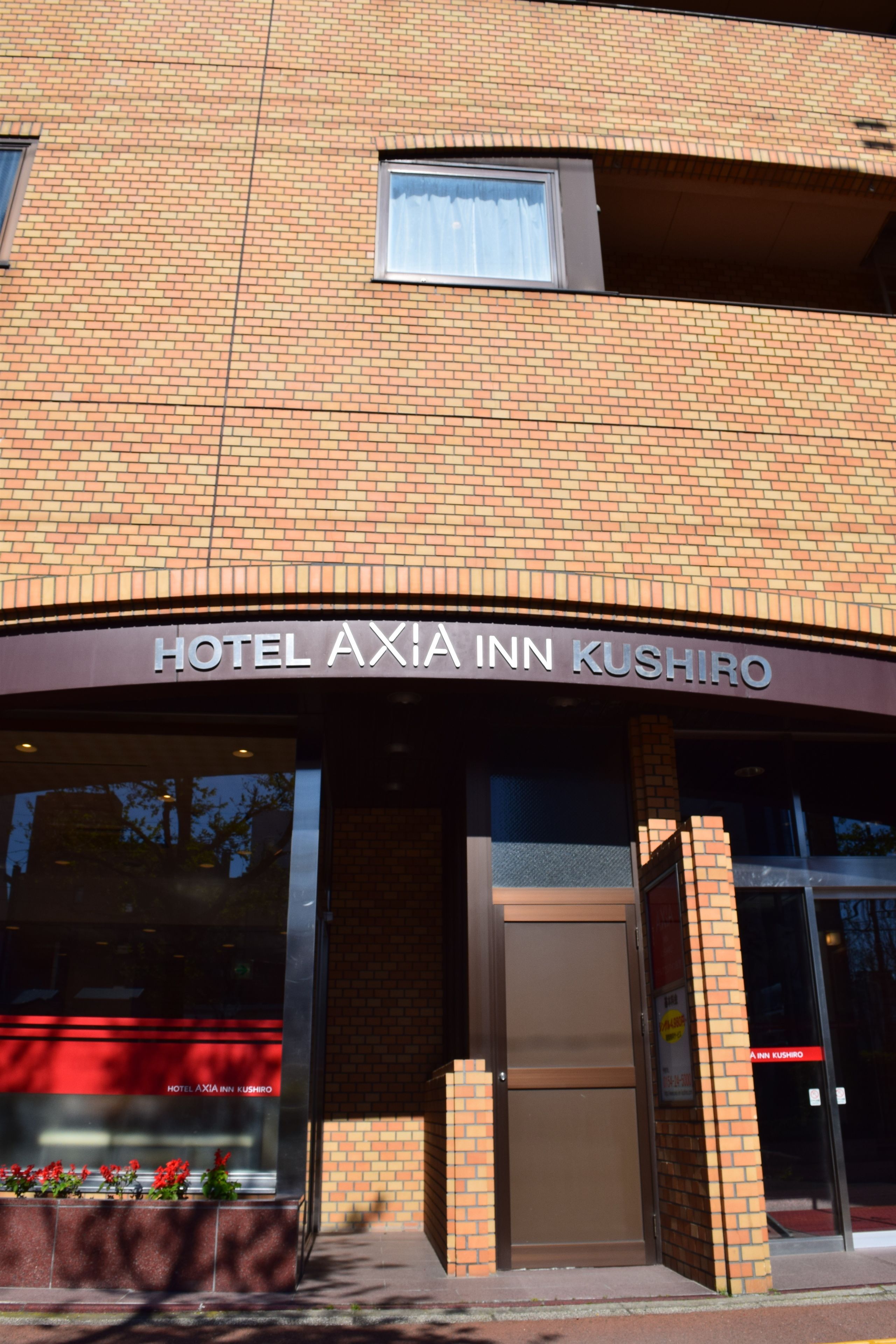 The exterior of Hotel Axia Inn Kushiro, featuring a brick facade, large windows, and a prominent entrance with a sign.