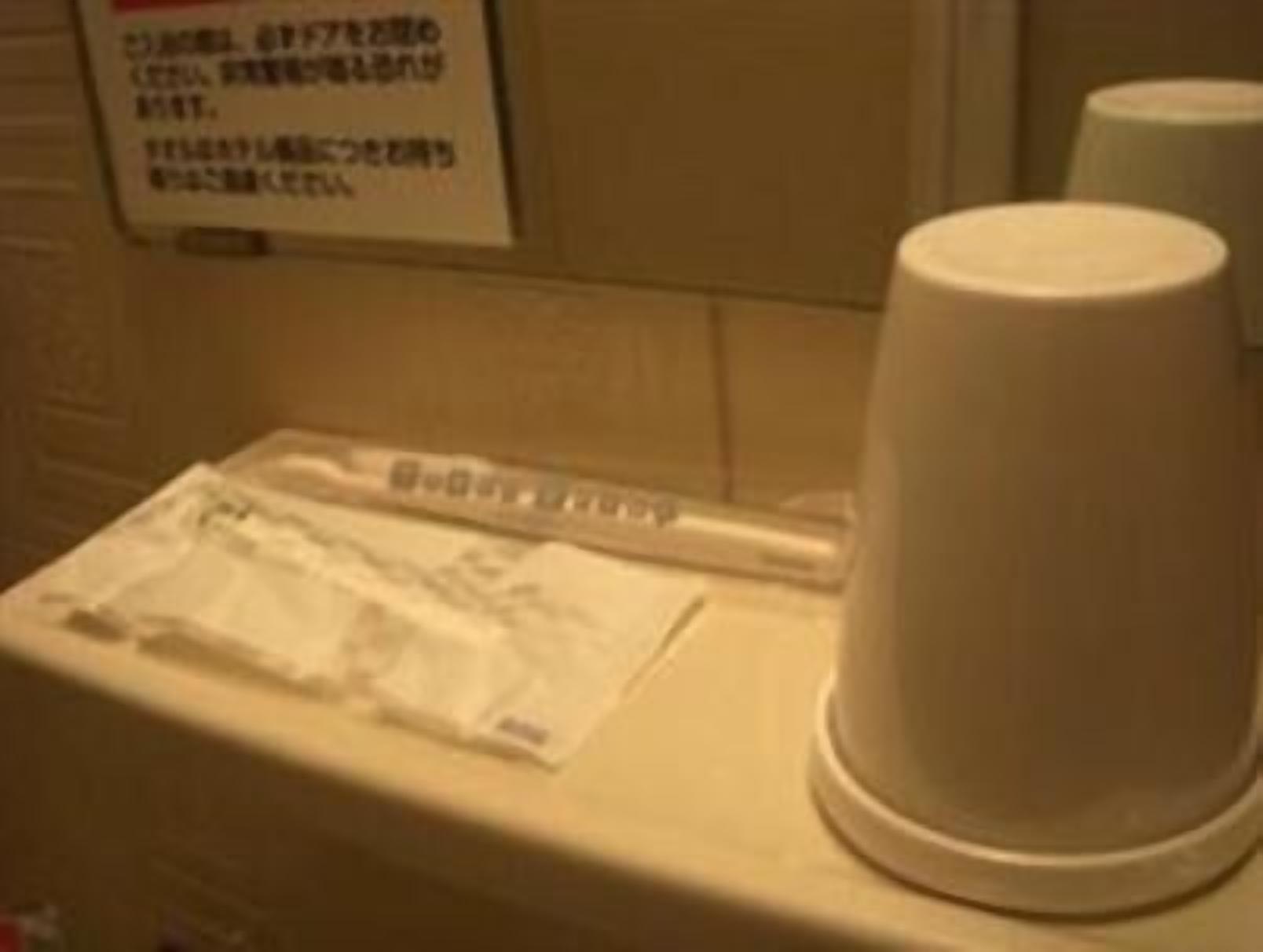 A restroom with a white urinal, a paper towel dispenser, and a sign with Japanese text.