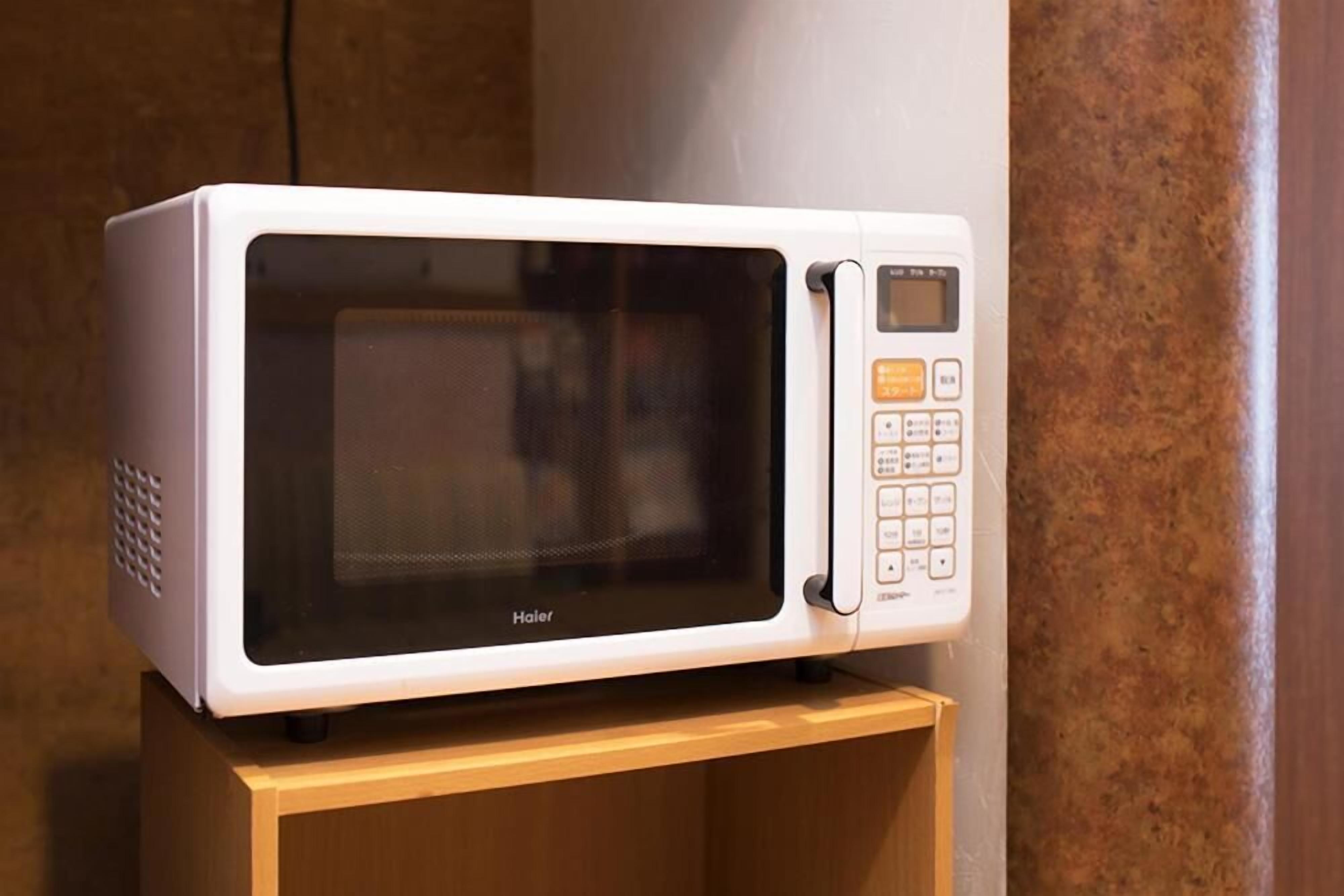 Un microondas blanco con pantalla digital y panel de control, sobre un pedestal de madera.