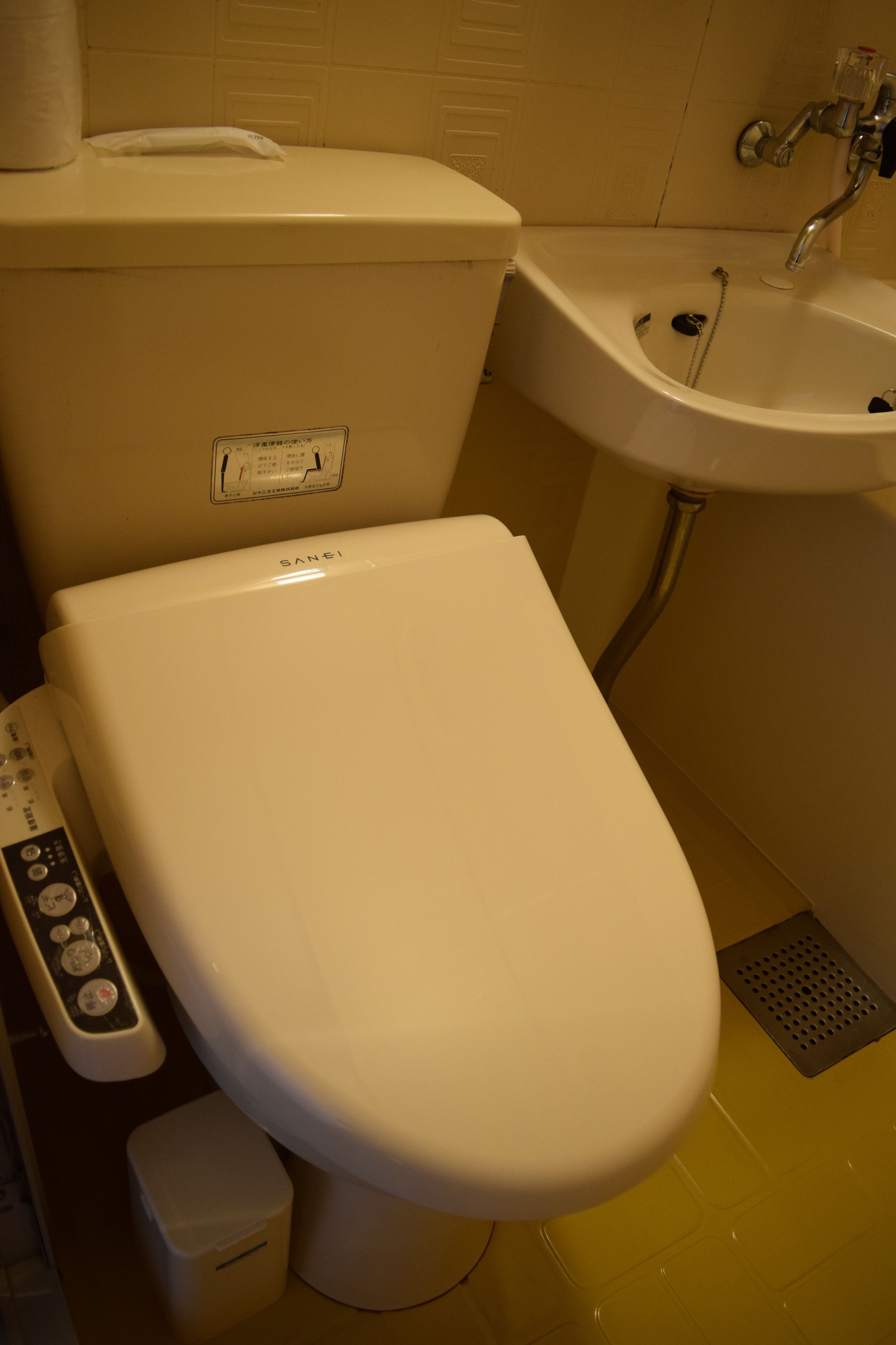 A toilet with a control panel, a small trash bin, and a sink with a faucet.