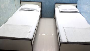Two single beds with white linens in a room with blue walls and a tiled floor.