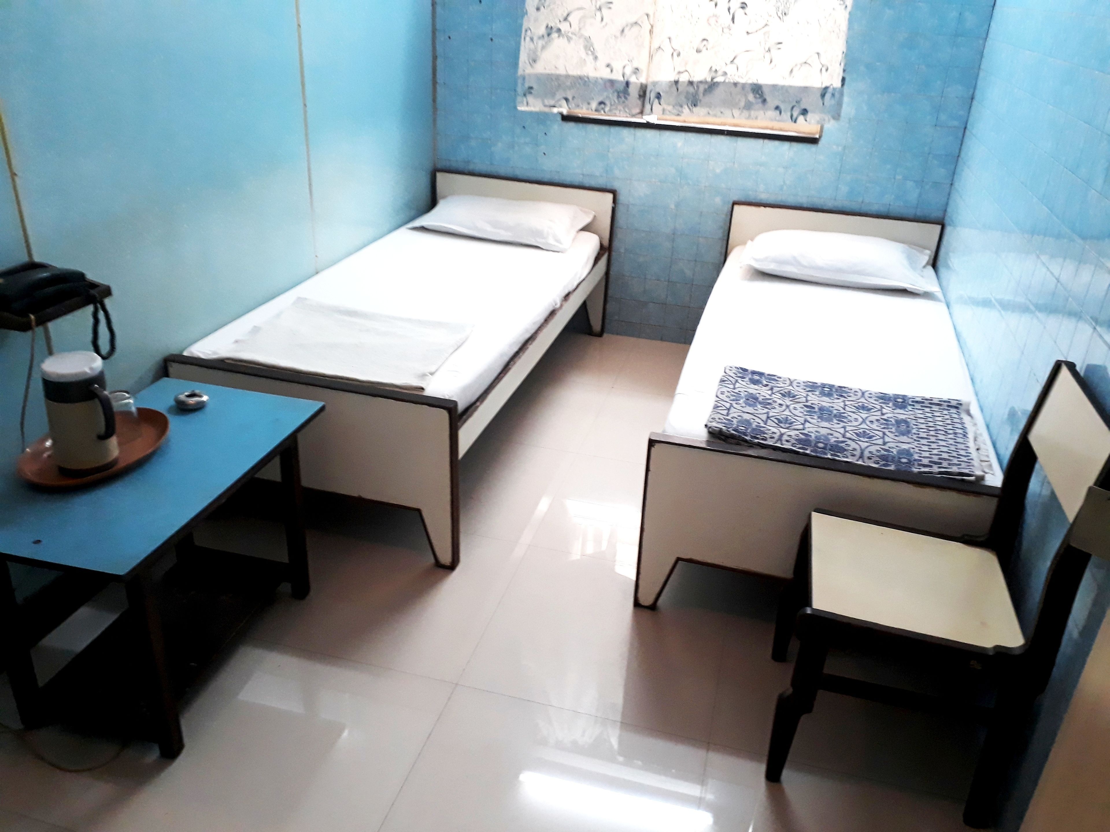 A small, clean room with two single beds, a desk with a chair, and a window with a patterned curtain.