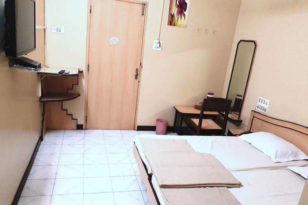 A hotel room with a bed, a desk, a chair, a television, and a door.