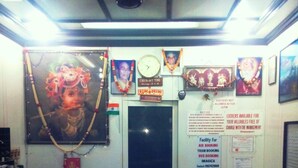 A reception desk with a clock, framed pictures, and a notice board. - Milan Guest House (Mumbai)