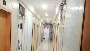 A long, narrow hallway with doors on both sides, leading to individual rooms. The floor is tiled, and the walls are painted in a light color. - Milan Guest House (Mumbai)
