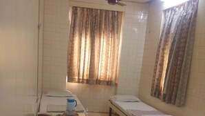 A room with two single beds, a ceiling fan, and a window with curtains. - Milan Guest House (Mumbai)