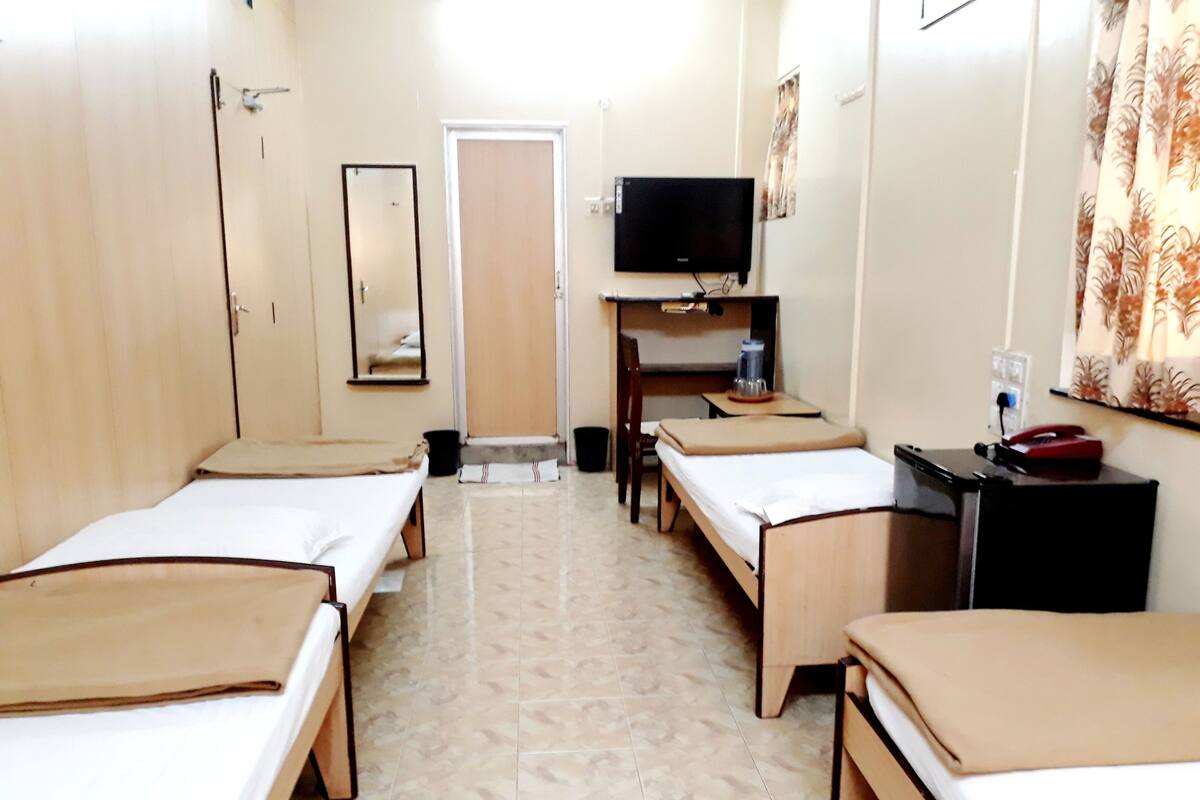 A hotel room with two single beds, a desk with a chair, a television, and a small table with a chair.