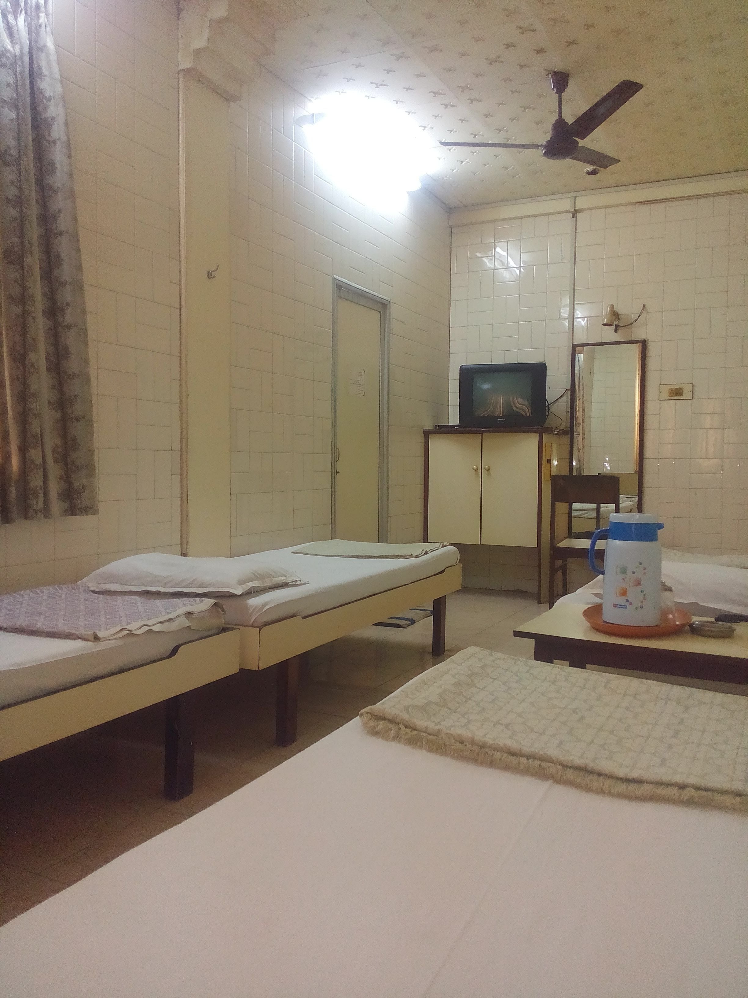 A room with two single beds, a television on a cabinet, a ceiling fan, and a mirror.