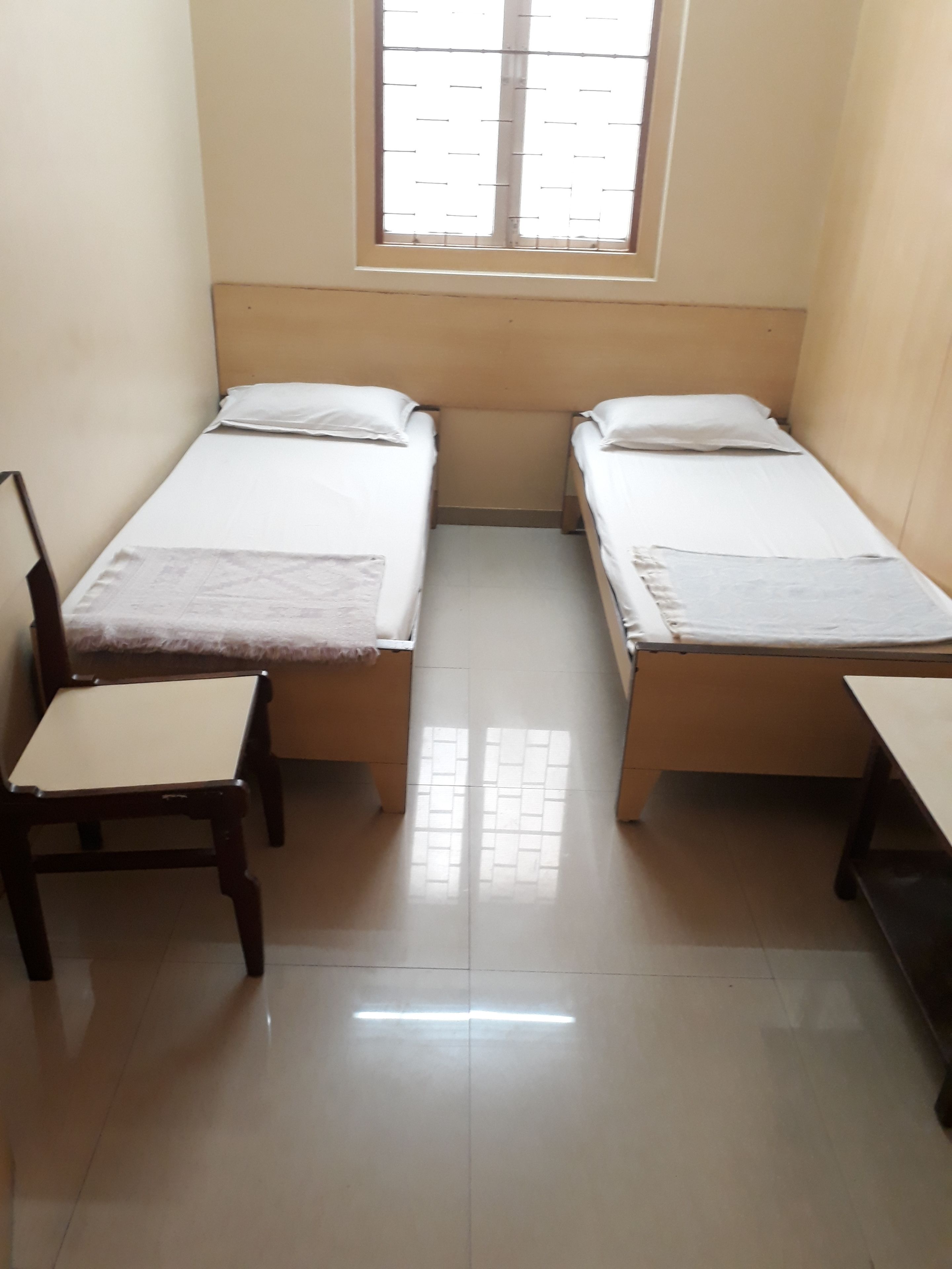 A small, clean room with two single beds, a wooden chair, and a desk.