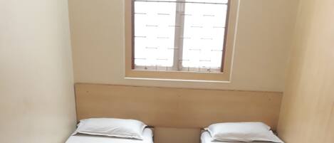 A small, clean room with two single beds, a wooden chair, and a desk.