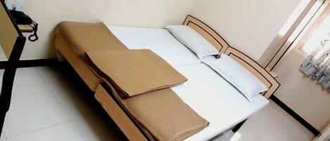 A neatly made bed with a wooden frame and white bedding, a desk with a chair, and a window with curtains.