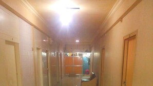 A long, narrow hallway with a shiny floor, a reception area with a counter and chairs, and a door on the right. - Sangam Guest House (Mumbai)