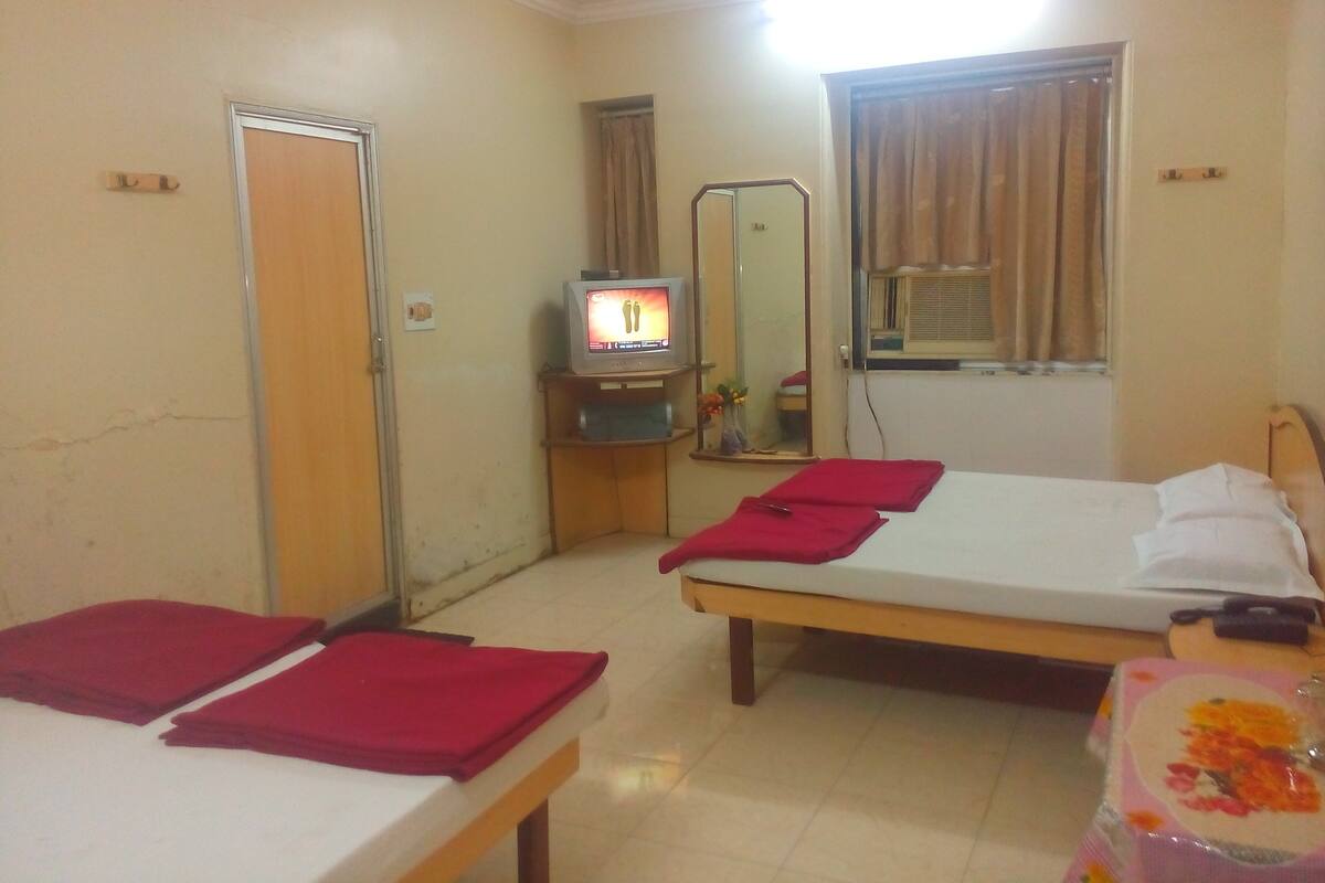 A hotel room with two beds, a TV on a small table, a mirror, and a window with curtains.
