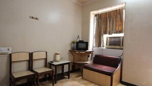 A small room with two wooden chairs, a small table, a television, and a window with curtains. - Sangam Guest House (Mumbai)