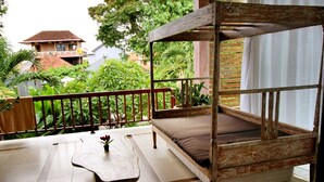 Un balcon avec un lit en bois, une petite table et une vue sur la verdure et les bâtiments environnants.