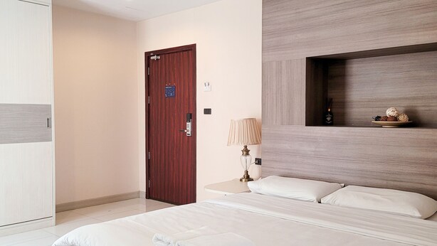 A modern hotel room with a large bed, a wooden door, a bedside table with a lamp, and a shelf with decorative items. - Parkview Ratchaprarop (Bangkok)