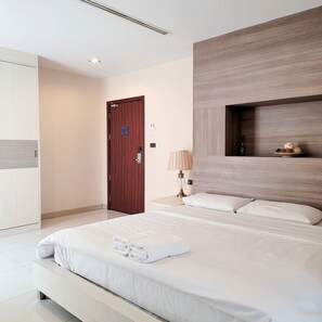 A modern hotel room with a large bed, a wooden door, a bedside table with a lamp, and a shelf with decorative items. - Parkview Ratchaprarop (Bangkok)