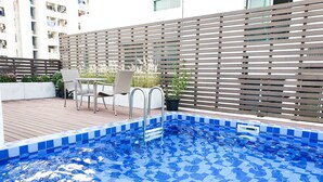 A swimming pool with blue tiles, a wooden deck, and outdoor furniture. - Parkview Ratchaprarop (Bangkok)