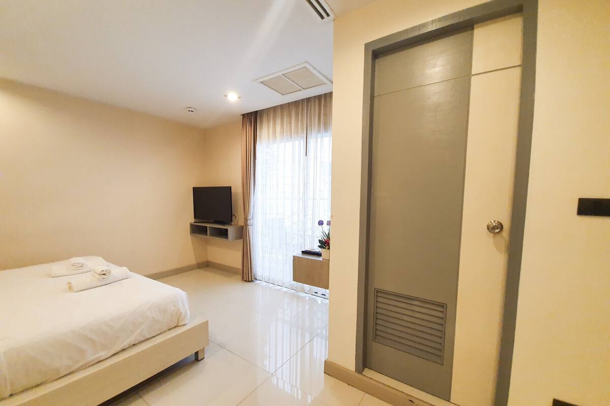 Una habitación de hotel con cama, televisión en la pared, una puerta y una ventana con cortinas.