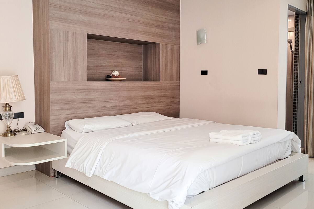 Un dormitorio moderno con una cama grande, una mesita de noche con lámpara y un estante empotrado con objetos decorativos.