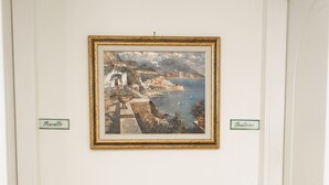 Un tavolo consolle in legno con un quadro che raffigura una scena costiera appeso sopra, una piccola ciotola e un certificato incorniciato sul tavolo.