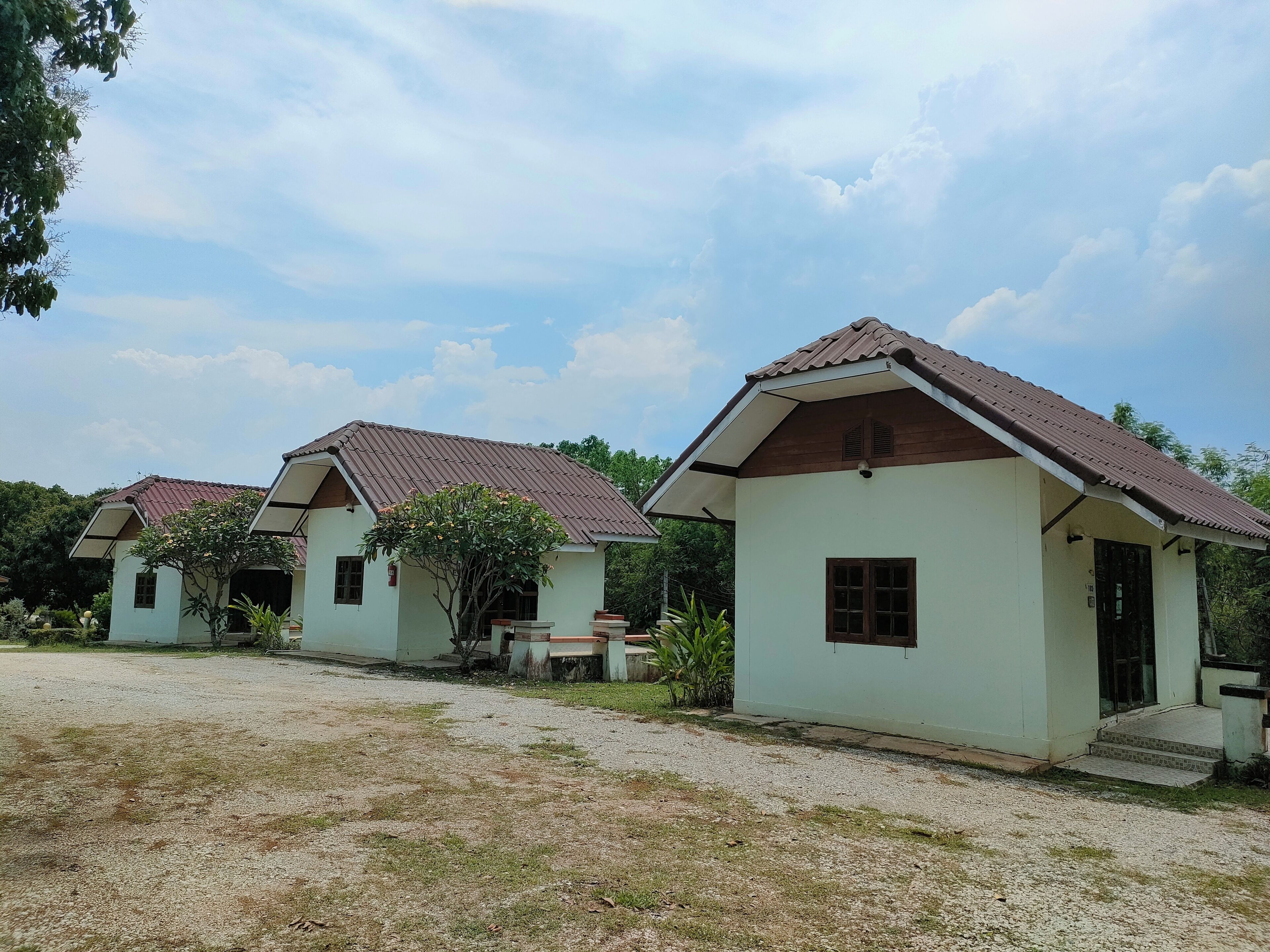 A row of small, single-story buildings with pitched roofs, surrounded by a gravel area and greenery.