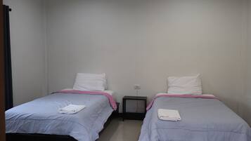 Dos camas individuales con almohadas blancas y colchas rosadas en una habitación pequeña y limpia con paredes blancas y piso de baldosas.