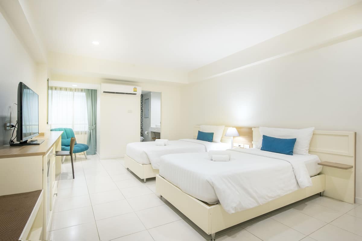 A hotel room with two beds, a desk, a chair, and a television.