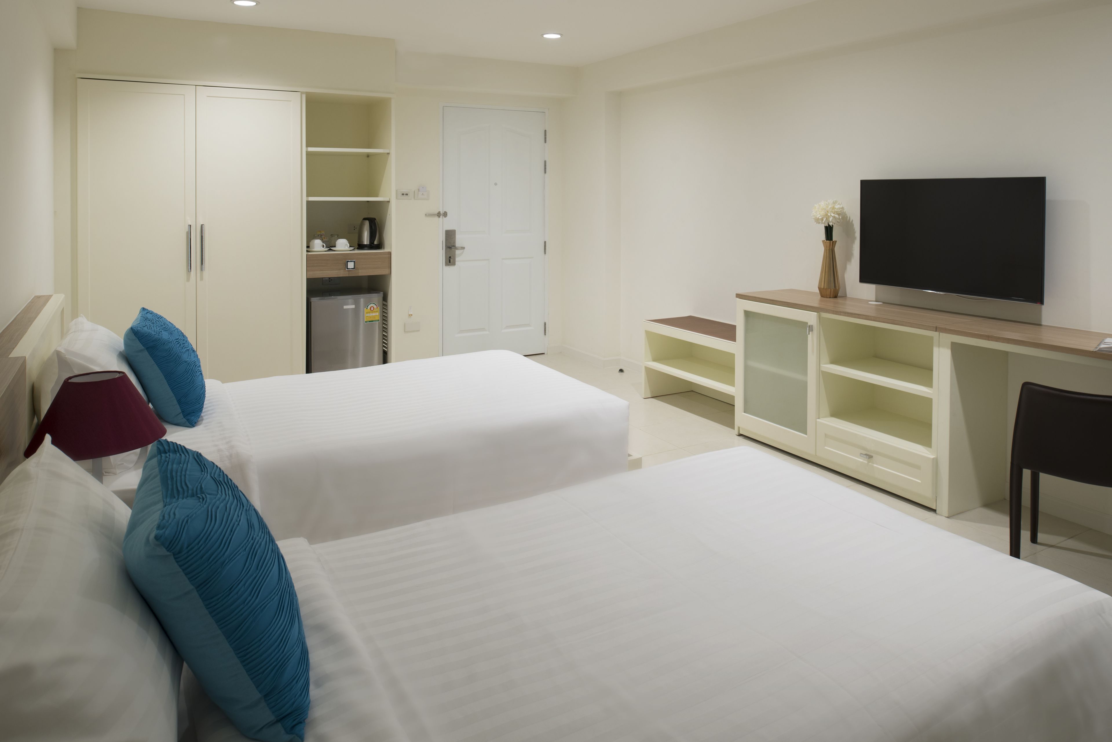 A hotel room with two beds, a TV, a desk, and a kitchenette.