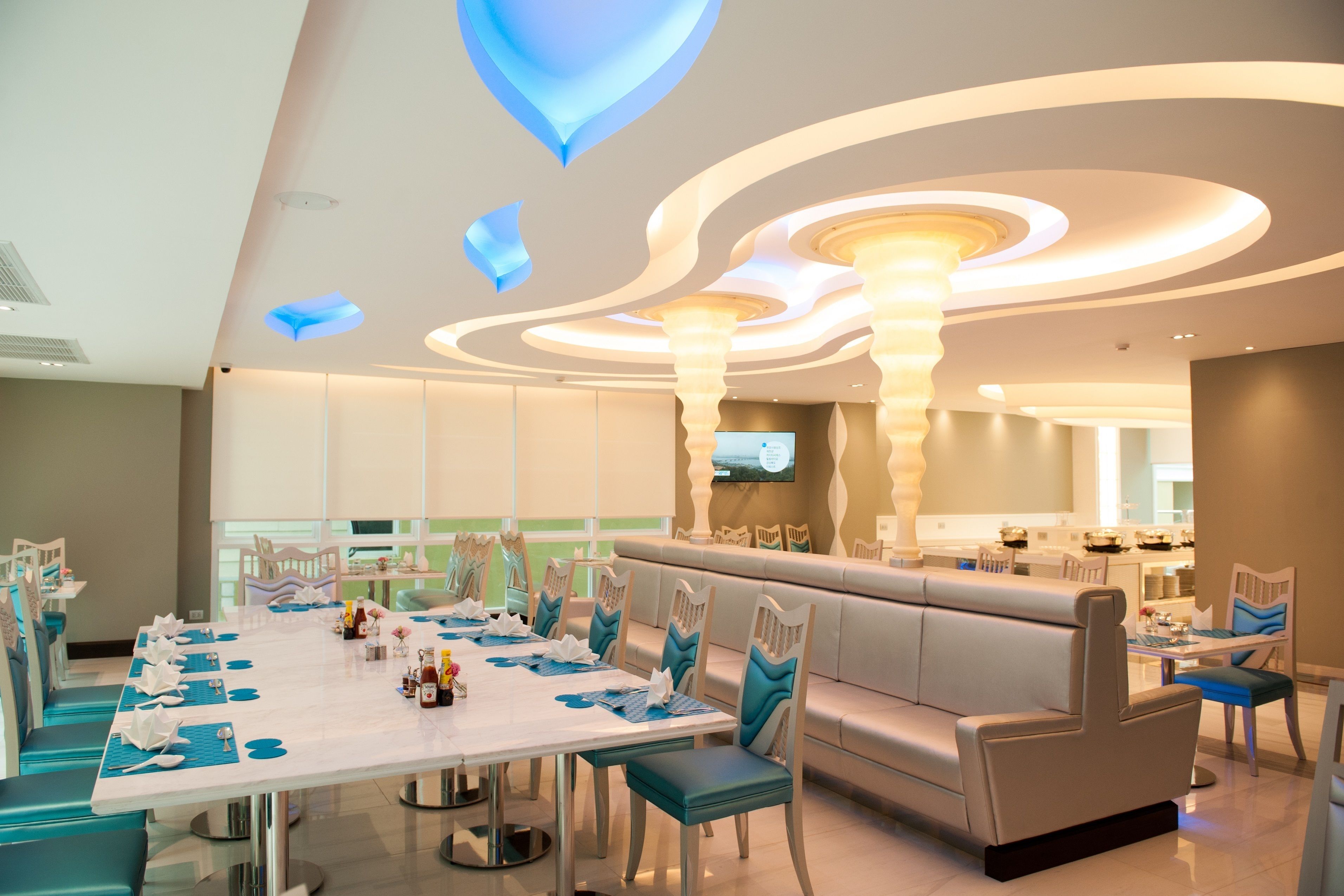 A modern dining area with a long table set for a meal, a comfortable seating area, and a kitchen in the background.