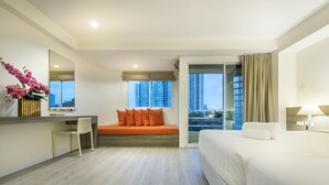 A hotel room with a bed, a desk, a chair, a sofa, a large window with a city view, and a mirror. - Le Tada Residence (Bangkok)
