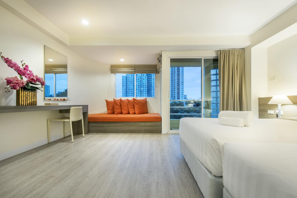 A hotel room with a bed, a desk, a chair, a sofa, a large window with a city view, and a mirror.