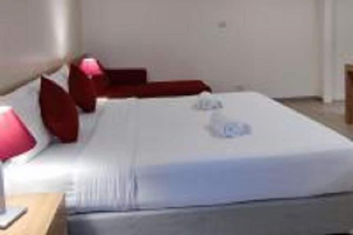 A hotel room with a large bed, red pillows, and a white headboard.