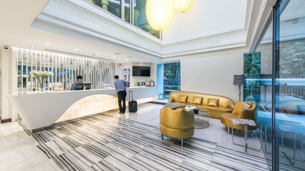 A modern lobby with a reception desk, a sofa, and a glass partition. - Le Tada Residence (Bangkok)
